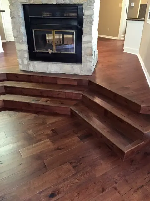 Dark hardwood flooring with custom stair steps around a stone fireplace