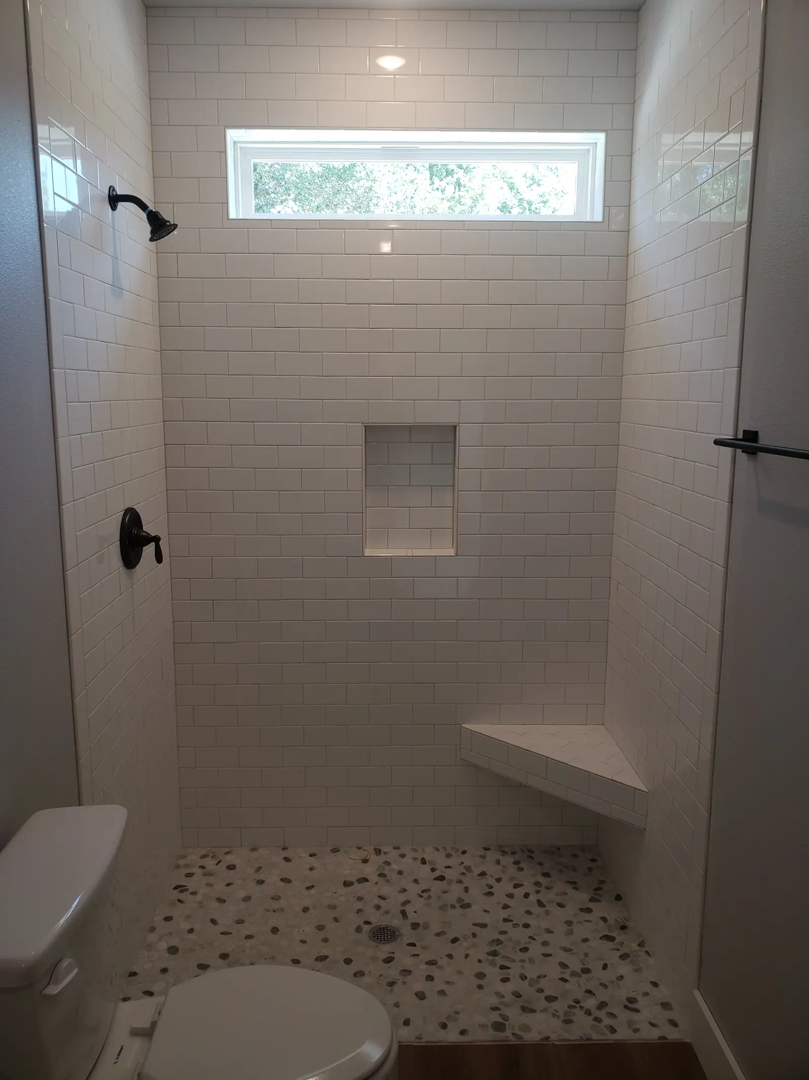 Subway tile shower with built-in bench and mosaic floor